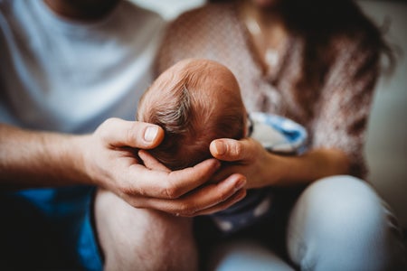 Young Mom and Dad sitting on a couch holding a newborn baby.