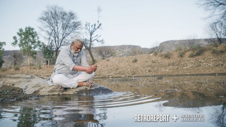 A man sits at a pool of water as the drops fall through cupped hands