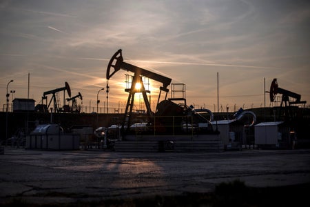 The sun sets beyond oil pumping units, also known as nodding donkeys or pump jacks, at an oil plant.