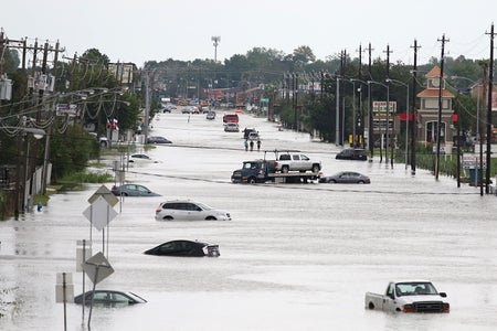 A car gets towed and others submerged in water while men walk in the flooded waters of Hurricane Harvey in Houston.