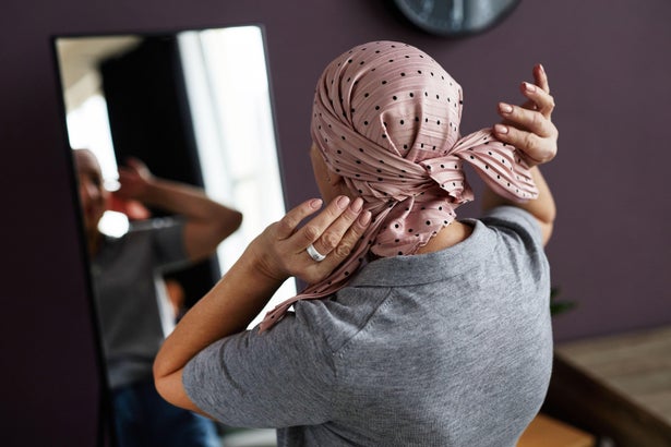 Back view of unrecognizable woman tying headscarf looking in mirror