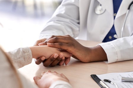 African female doctor holds hand of caucasian woman patient to give comfort.