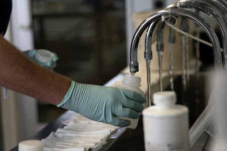 Person with green glove ollects samples of treated Lake Michigan water in a laboratory sampling water at a water treatment plant.