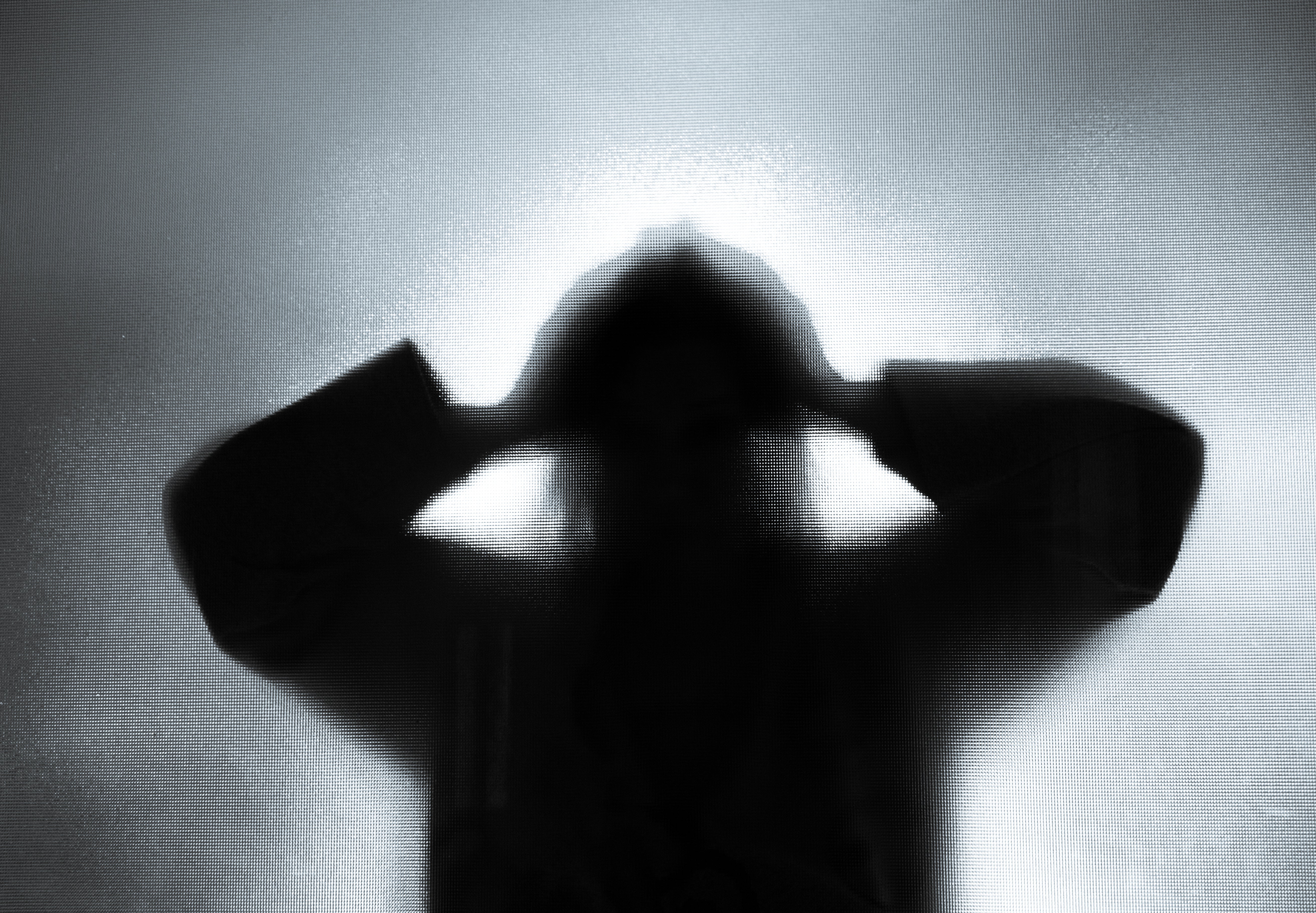 Silhouette of a woman lifting arms and holding her head in her hands in despair.