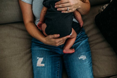 Overhead photograph of a woman wearing a wedding ring, sitting on a couch, holding a baby