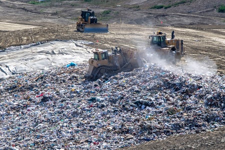 Three yellow trucks distributing trash in a landfill.