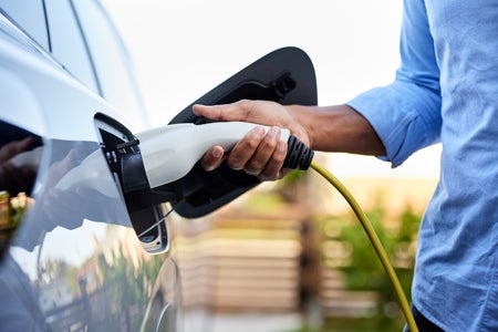 Close-up view of a person's hand plugging in charger to electric vehicle.