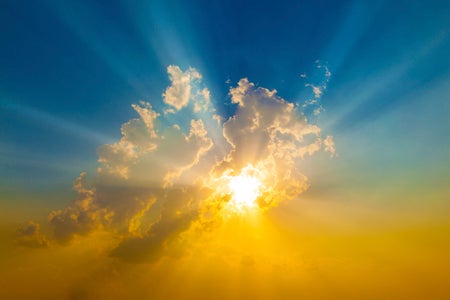 A view of the sky showing the sun behind a cloud.