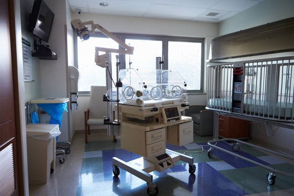 An empty infant incubator in a hospital room in front of a window