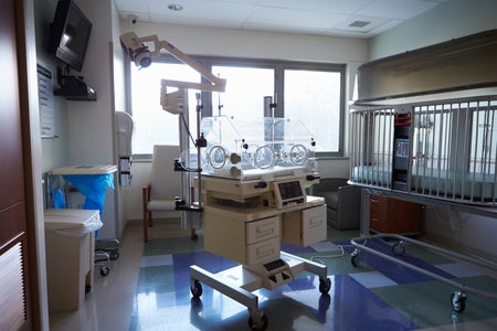 An empty infant incubator in a hospital room in front of a window