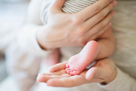 Mid section of woman with hands holding baby's back and foot.